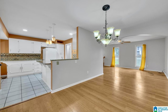 kitchen featuring light wood-type flooring, ceiling fan with notable chandelier, kitchen peninsula, white cabinetry, and white fridge