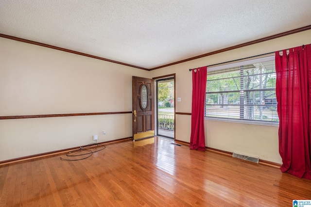 spare room featuring crown molding, a textured ceiling, and light wood-type flooring