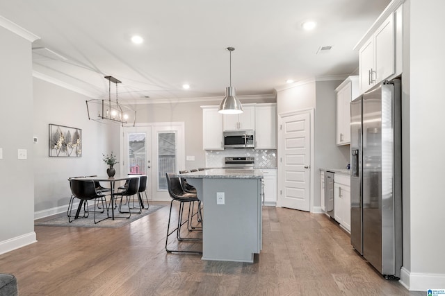 kitchen with wood-type flooring, a center island, pendant lighting, white cabinetry, and appliances with stainless steel finishes