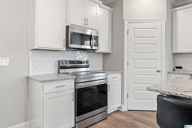 kitchen with white cabinets, tasteful backsplash, appliances with stainless steel finishes, light stone countertops, and light hardwood / wood-style floors