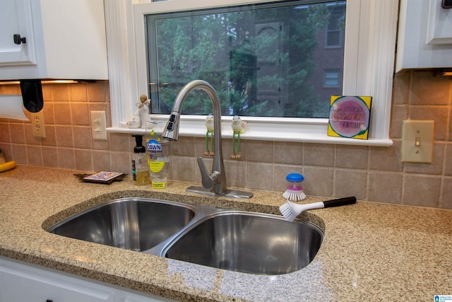 interior details featuring white cabinets, decorative backsplash, sink, and light stone countertops