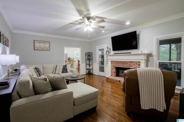 living room featuring dark wood-type flooring, ceiling fan, ornamental molding, and a brick fireplace