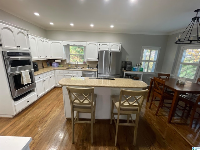 kitchen with stainless steel appliances, white cabinetry, sink, decorative light fixtures, and a center island