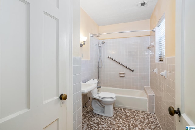 bathroom featuring tiled shower / bath, tile walls, tile patterned floors, and toilet