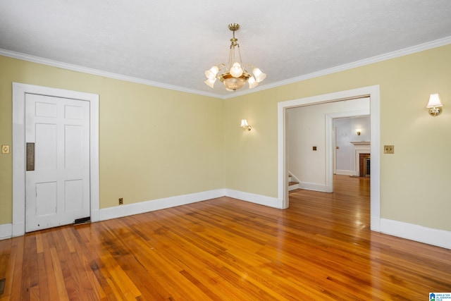 empty room with ornamental molding, hardwood / wood-style floors, a brick fireplace, and a notable chandelier