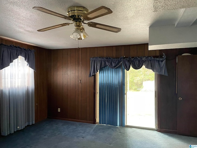 carpeted spare room featuring ceiling fan, a textured ceiling, and wooden walls