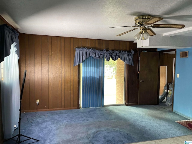 carpeted spare room featuring ceiling fan, a textured ceiling, and wood walls