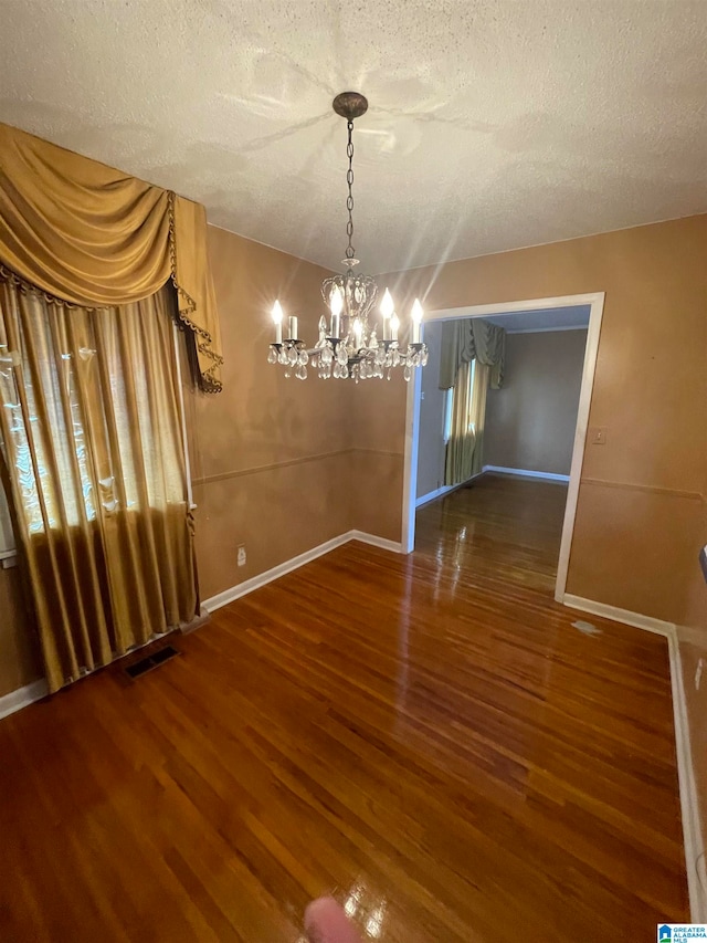 unfurnished dining area featuring a notable chandelier, a textured ceiling, and hardwood / wood-style flooring