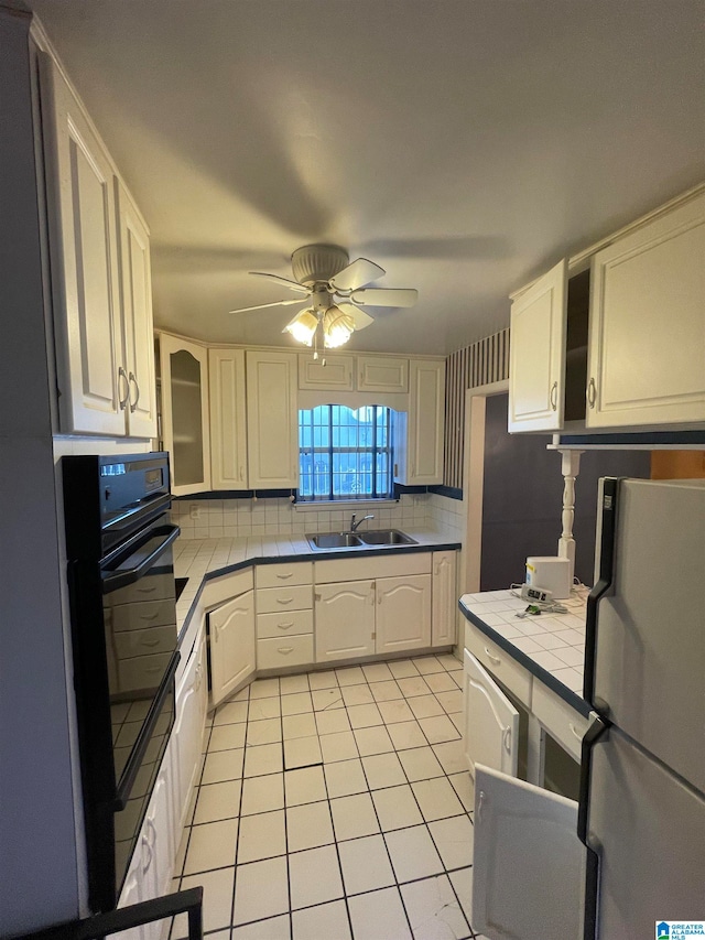 kitchen with backsplash, tile countertops, black oven, white fridge, and sink