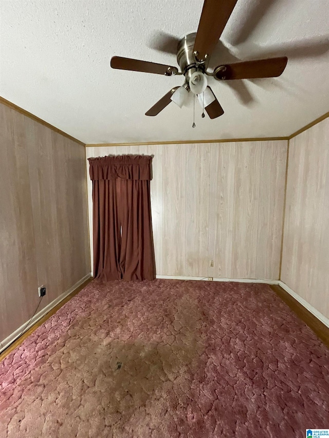 spare room with wood walls, a textured ceiling, dark carpet, and ceiling fan