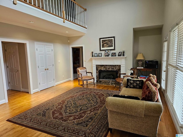 living room featuring a premium fireplace, light hardwood / wood-style floors, ornamental molding, and a towering ceiling