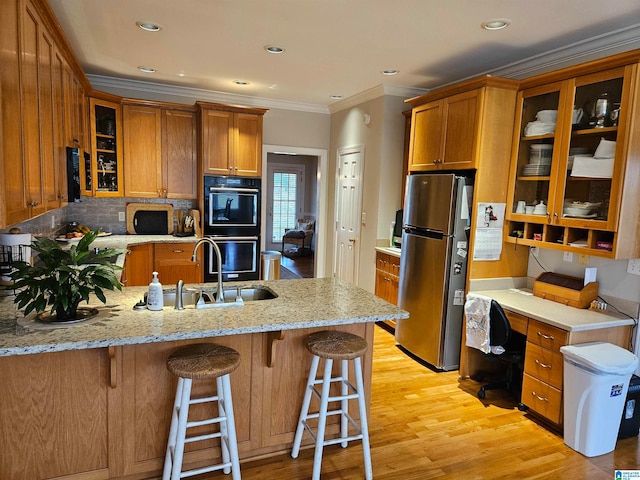 kitchen featuring ornamental molding, sink, stainless steel fridge, black double oven, and light hardwood / wood-style floors