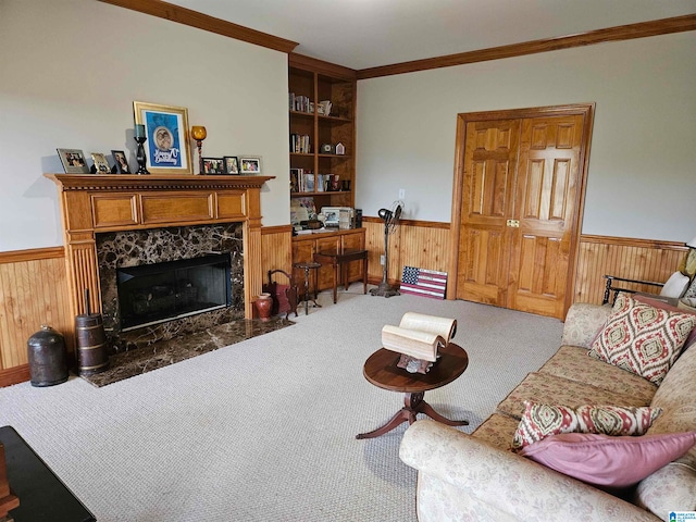 carpeted living room featuring crown molding, wooden walls, a fireplace, and built in shelves