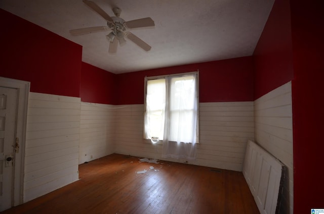 empty room featuring radiator, ceiling fan, wood walls, and wood-type flooring