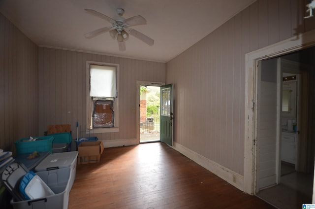 interior space with ceiling fan, wood-type flooring, ornamental molding, and wooden walls