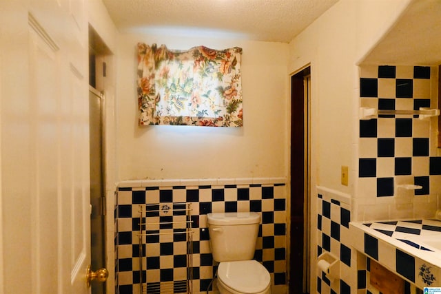 bathroom with toilet, tile walls, and a textured ceiling