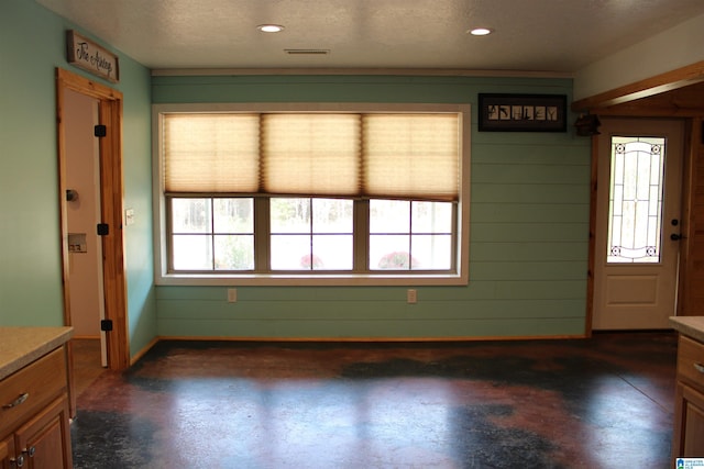 interior space with a textured ceiling, a wealth of natural light, and wood walls