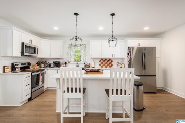 kitchen with hanging light fixtures, a kitchen island, appliances with stainless steel finishes, white cabinetry, and light hardwood / wood-style floors