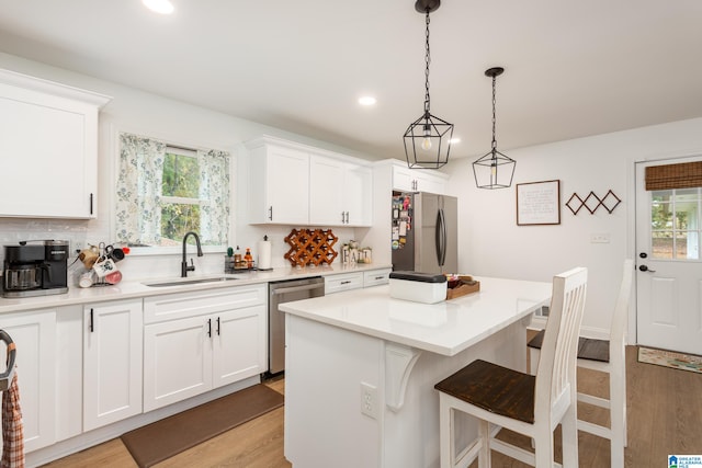 kitchen with stainless steel appliances, sink, a center island, light wood-type flooring, and white cabinetry