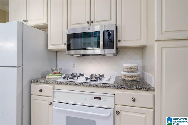 kitchen featuring decorative backsplash, white cabinetry, white appliances, and dark stone countertops