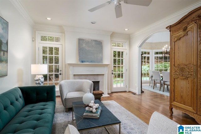 living room featuring wood-type flooring, ornamental molding, and ceiling fan with notable chandelier