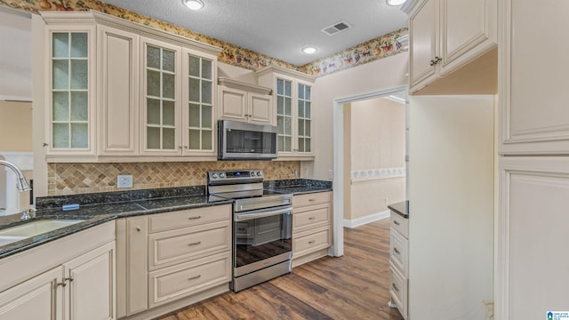 kitchen with appliances with stainless steel finishes, backsplash, a textured ceiling, hardwood / wood-style floors, and dark stone countertops