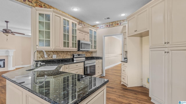 kitchen featuring kitchen peninsula, dark stone countertops, sink, appliances with stainless steel finishes, and light hardwood / wood-style floors