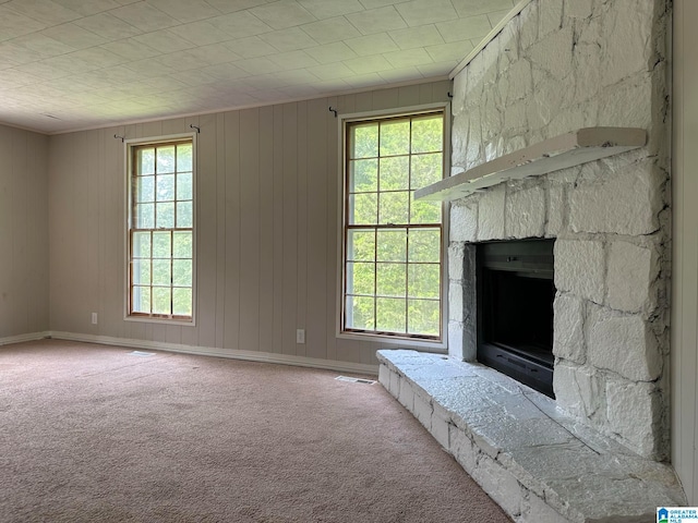 unfurnished living room with carpet, a stone fireplace, crown molding, and wooden walls