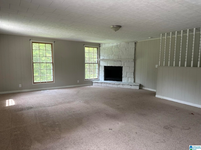 unfurnished living room with a stone fireplace, a wealth of natural light, and carpet floors