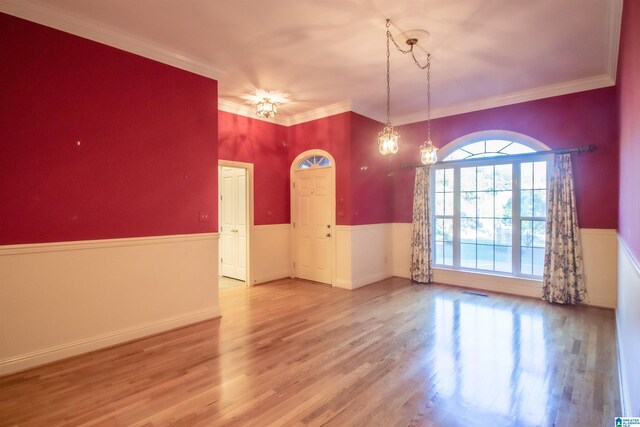 empty room with wood-type flooring, an inviting chandelier, and ornamental molding