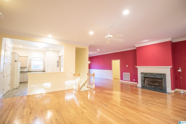 unfurnished living room with ceiling fan, a high end fireplace, light wood-type flooring, and crown molding