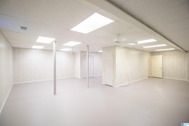 basement with a drop ceiling, wood walls, and ceiling fan