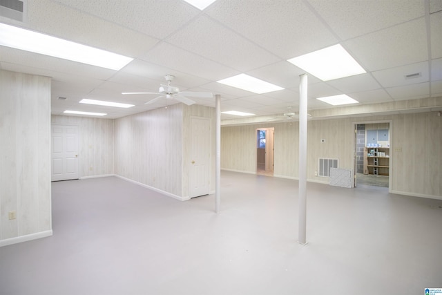 basement with wood walls, ceiling fan, and a drop ceiling