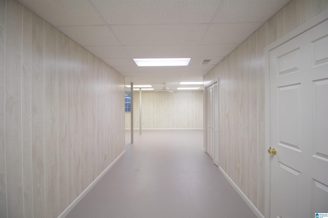 hallway with a drop ceiling, concrete flooring, and wood walls