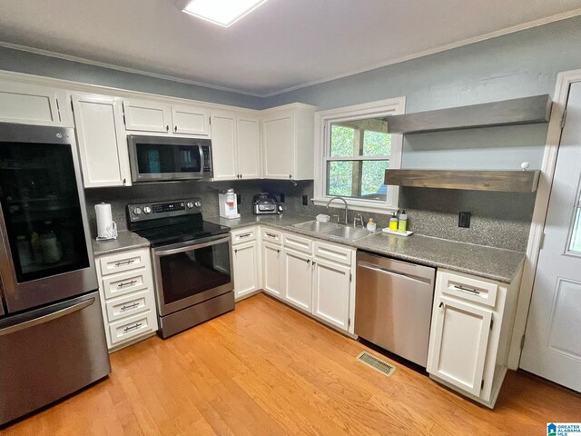 kitchen with white cabinets, appliances with stainless steel finishes, ornamental molding, and sink