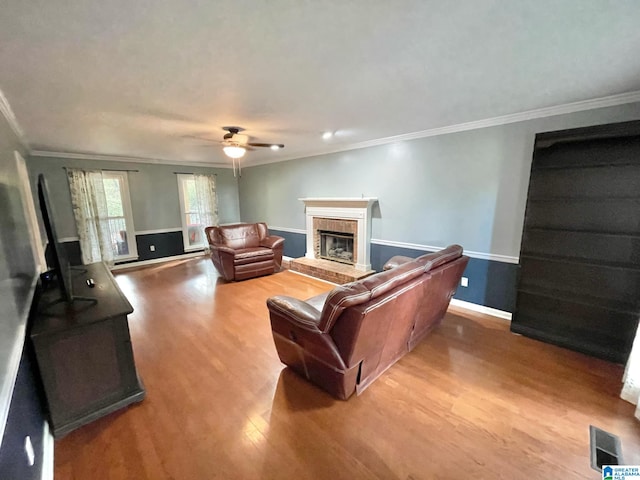 living room with light wood-type flooring, ceiling fan, crown molding, and a brick fireplace