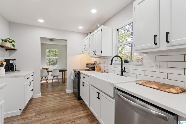 kitchen with stainless steel dishwasher, hardwood / wood-style flooring, white cabinetry, and black electric range oven