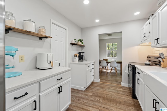 kitchen featuring tasteful backsplash, black range with electric cooktop, light stone countertops, white cabinetry, and light hardwood / wood-style flooring