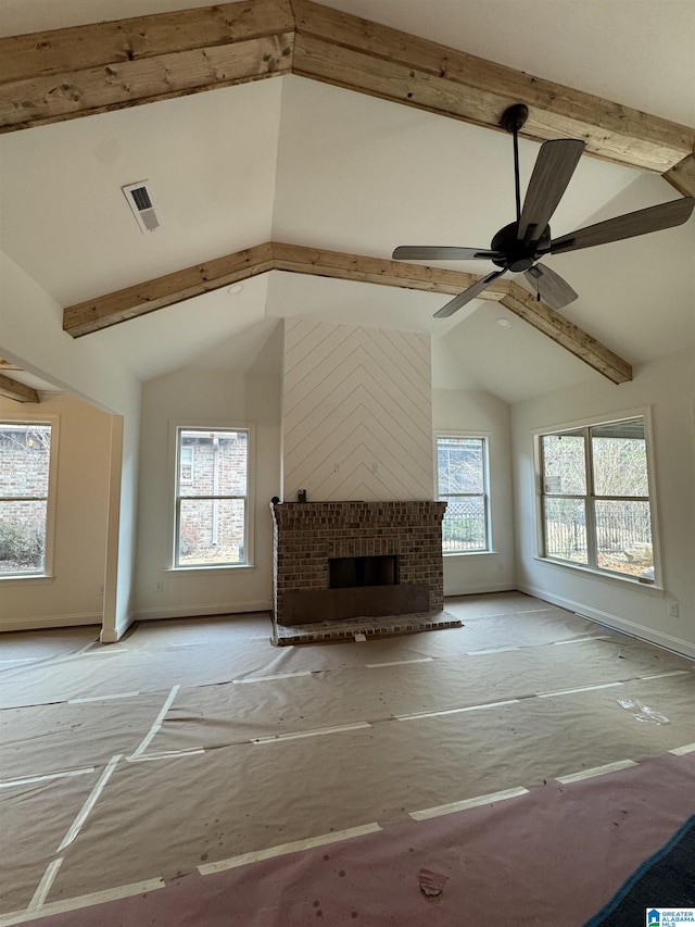 unfurnished living room with ceiling fan, a healthy amount of sunlight, lofted ceiling with beams, and a brick fireplace