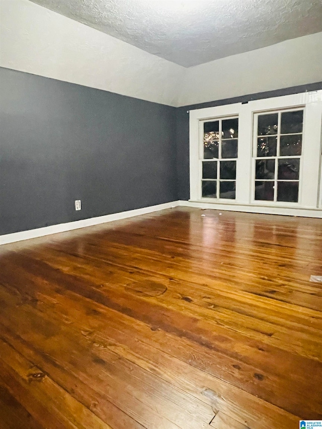 spare room with lofted ceiling, a textured ceiling, and hardwood / wood-style flooring