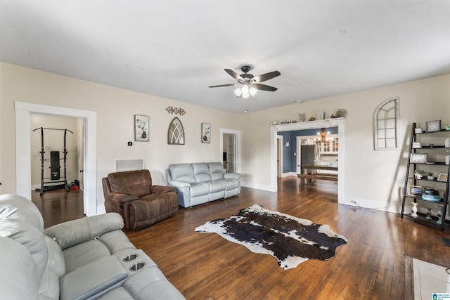 living room with ceiling fan with notable chandelier and dark hardwood / wood-style flooring