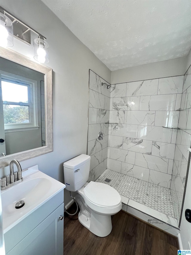 bathroom featuring hardwood / wood-style floors, vanity, toilet, and a tile shower