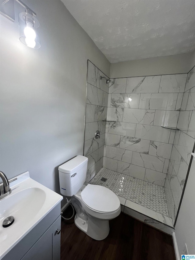 bathroom with tiled shower, hardwood / wood-style flooring, toilet, and vanity