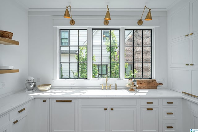 kitchen featuring white cabinetry, sink, crown molding, and light stone countertops