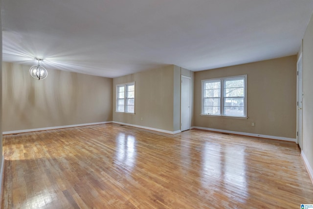 empty room with a wealth of natural light, light hardwood / wood-style floors, and an inviting chandelier