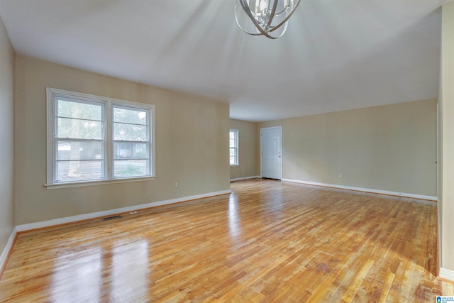 unfurnished living room featuring a wealth of natural light, an inviting chandelier, and light hardwood / wood-style floors