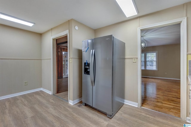 kitchen with wood walls, stainless steel refrigerator with ice dispenser, and light hardwood / wood-style flooring