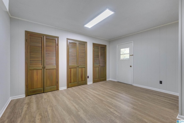 interior space featuring multiple closets, ornamental molding, and light hardwood / wood-style flooring