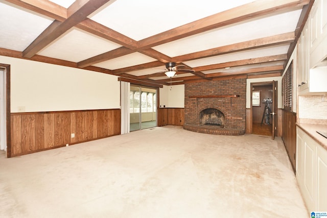 unfurnished living room with beamed ceiling, wooden walls, light colored carpet, and a brick fireplace