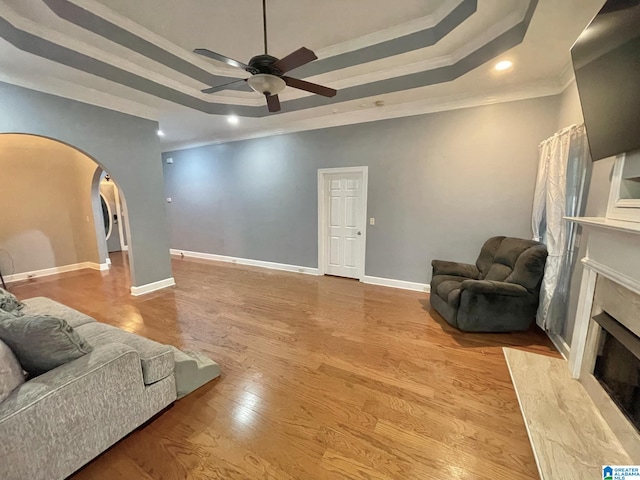 living room featuring crown molding, light wood-type flooring, a raised ceiling, a premium fireplace, and ceiling fan